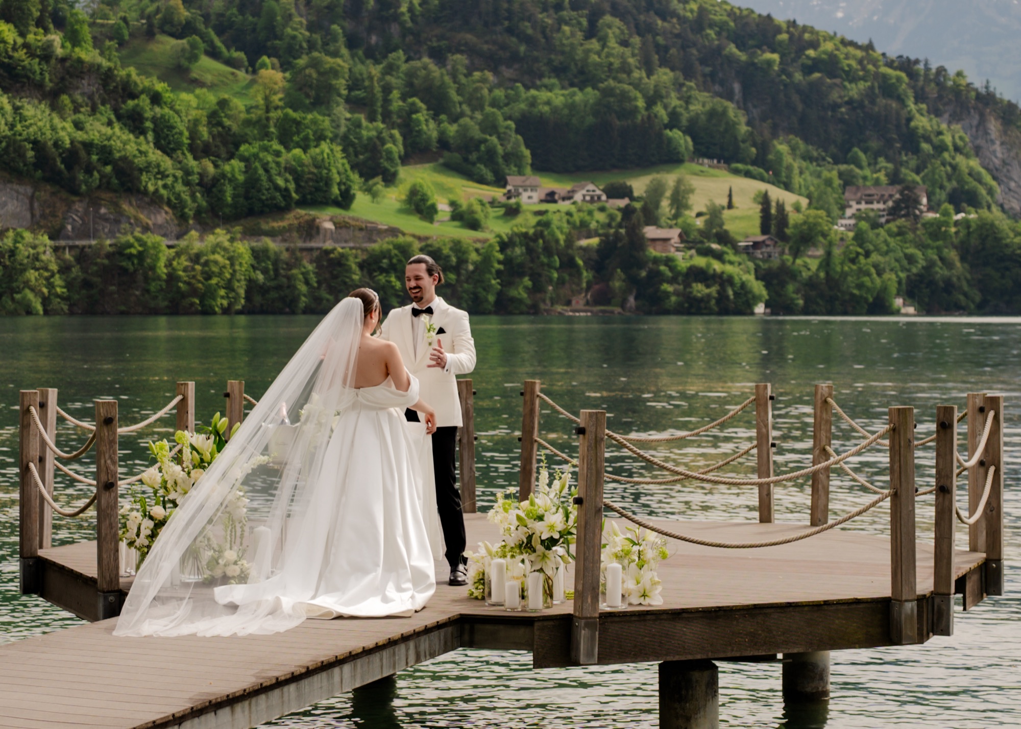 Brautpaar auf einem Holzsteg vor See und Bergen